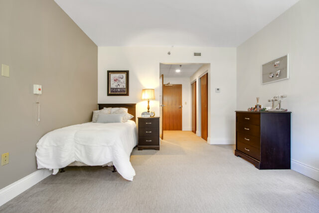 wide view of deluxe private room including dresser, bed and hallway